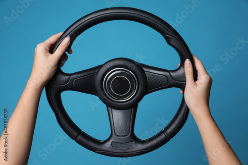 Fototapet Woman holding steering wheel on blue background, closeup