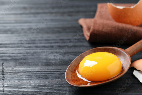 Obraz na płótnie Spoon with raw egg yolk on black wooden table, closeup