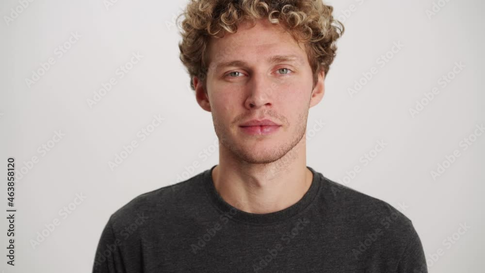 Smiling curly-haired man opening his eyes at the camera in white studio Smiling curly-haired man opening his eyes at the camera in white studio