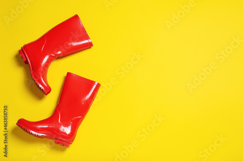 Pair of red rubber boots on yellow background, top view. Space for text