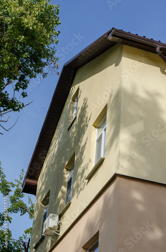 A yellow and pink house against a blue sky. Brown roof with drai photo