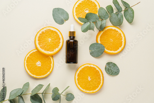 Vitamin C serum in cosmetic transparent bottle with dropper, sliced orange  and eucalyptus leaves, top view. Facial skin care concept. Natural organic cosmetics beauty