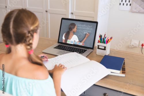 Caucasian girl using laptop for video call, with african american female teacher on screen