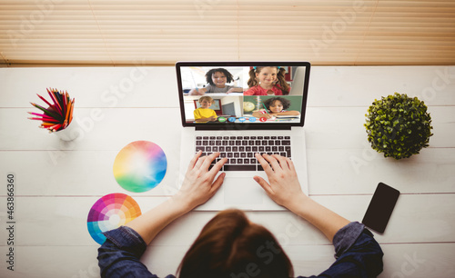 Caucasian girl using laptop for video call, with smiling diverse elementary school pupils on screen