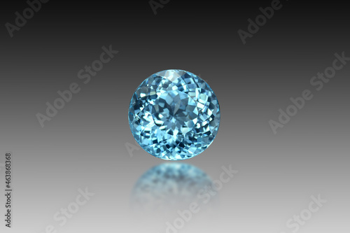 Natural Swiss blue topaz gemstone loose faceted setting for making jewelry. Round shape. Front view. Gray gradient background, blury half reflection effect. Isolated. Gemology theme. Irradiated stone.