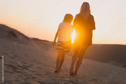 woman and her child walking on sand dunes at sunrise