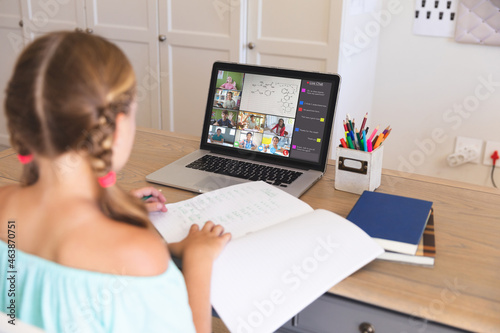 Caucasian girl using laptop for video call, with diverse elementary school pupils on screen