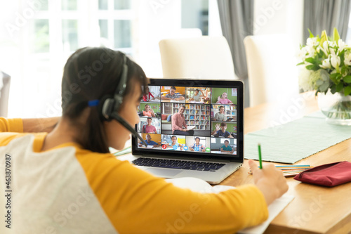 Asian girl using laptop for video call, with diverse elementary school pupils on screen photo