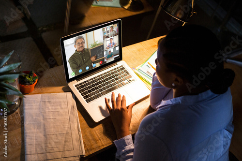 African american woman using laptop for video call, with diverse elementary school pupils on screen photo