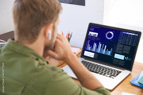Caucasian businessman sitting at desk using laptop with graph and statistical data on screen photo