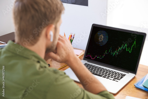 Caucasian businessman sitting at desk using laptop with graph and statistical data on screen photo
