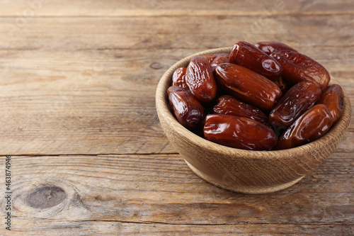 Sweet dried dates in bowl on wooden table. Space for text