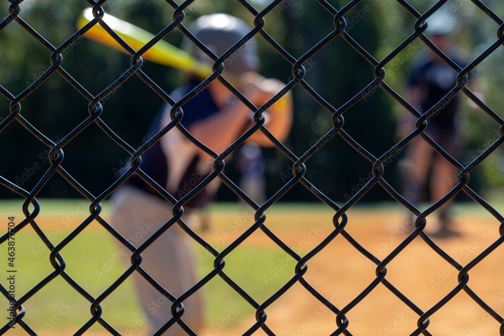 Little league batter out of focus in the background while the backstop is in focus Little league batter out of focus in the background while the backstop is in focus