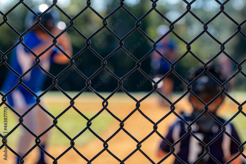 Little league batter out of focus in the background while the backstop is in focus Little league batter out of focus in the background while the backstop is in focus