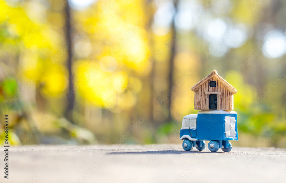 Toy truck carrying a tiny house against a forest background - obrazy, fototapety, plakaty 