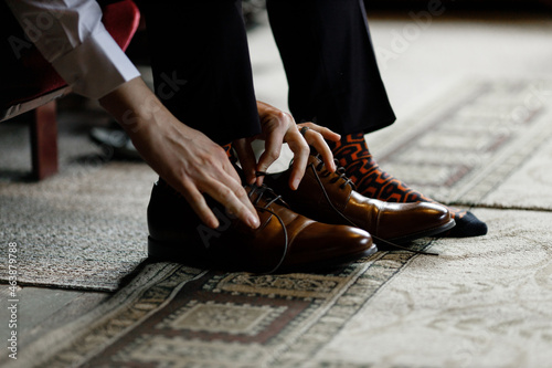 The guy is tying the laces on brown classic shoes Side view The groom wears nice shoes and ties his shoelaces Close-up 