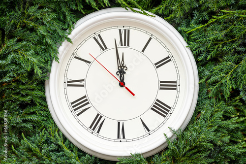 White round vintage clock with black digits and hands lying on evergreen fir tree branches as background for Christmas decor