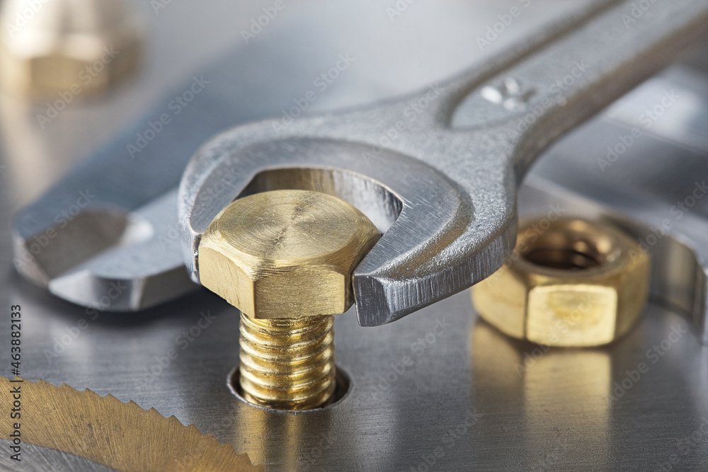 Wrench tightens brass bolt in steel billet. Spanner, bolt, screw and nuts. Wrench tightens brass bolt in steel billet. Spanner, bolt, screw and nuts.