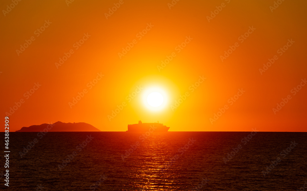 A backlit passenger ship near an island at sunset