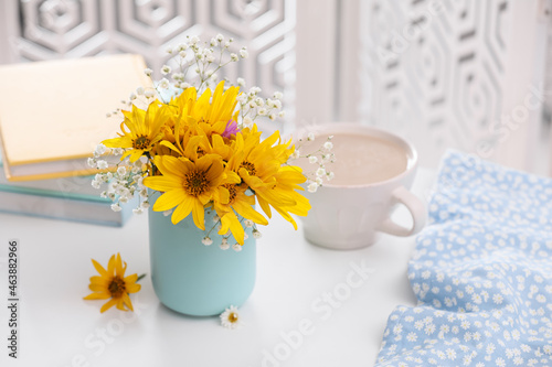 Beautiful bright flowers, cup of coffee and fabric on white table. Space for text