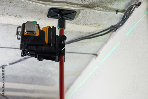 Laser level measuring tool with visible green laser beam on wall for installing stretch ceiling photo