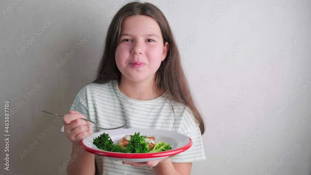 Brunette girl eating broccoli with fish. Healthy baby food concept.