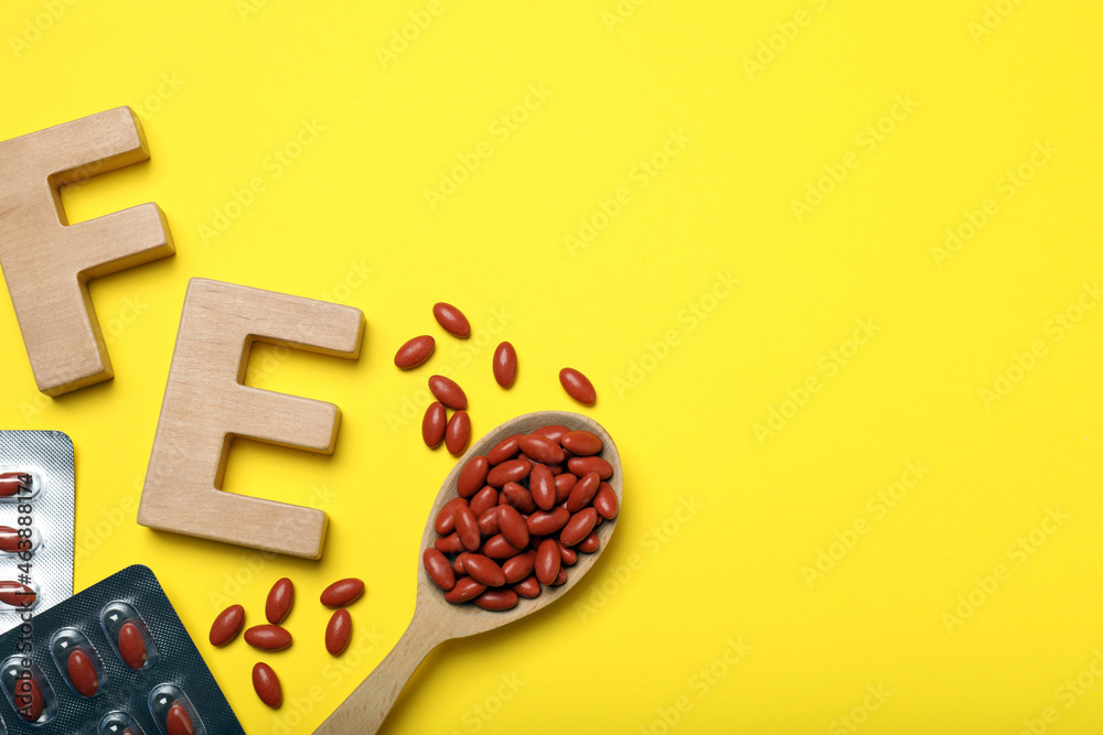 Wooden letters FE and pills on yellow background, flat lay with space for text. Anemia treatment - obrazy, fototapety, plakaty 