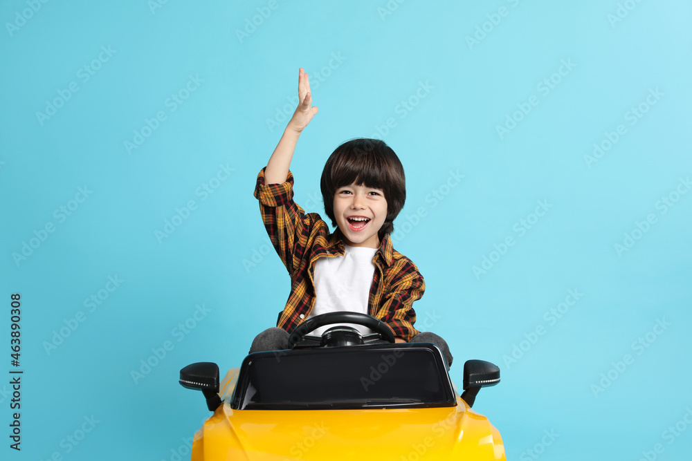 Little child driving yellow toy car on light blue background Little child driving yellow toy car on light blue background