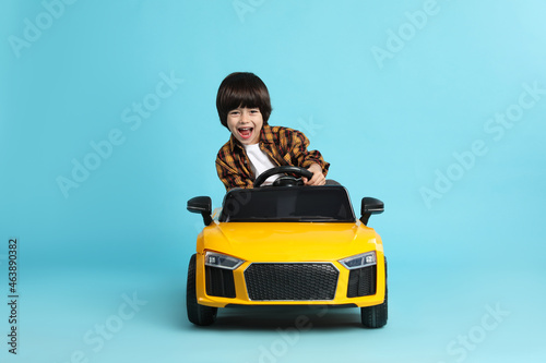 Little child driving yellow toy car on light blue background