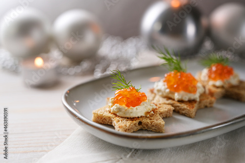 Holiday canapes with red caviar, cream and dill garnish on toasted bread in star shape on a gray plate, festive silver Christmas decoration, copy space