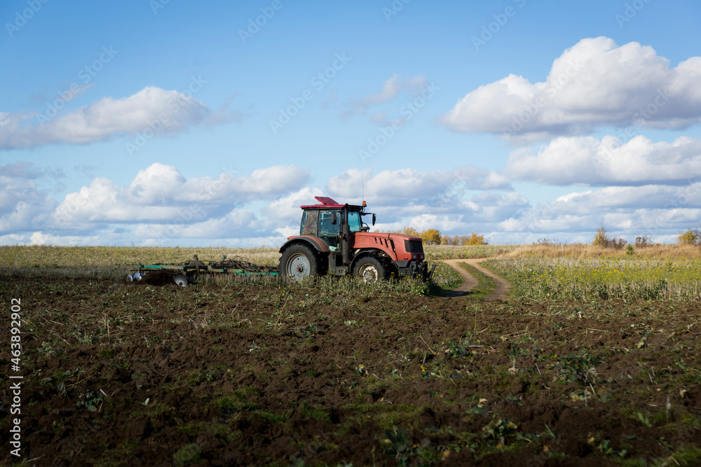 Obraz premium A farmer in a tractor, agricultural machinery, prepares the land with a cultivator. A modern red tractor in a field. Plowing a heavy tractor while cultivating agricultural work in a field with a plow.
