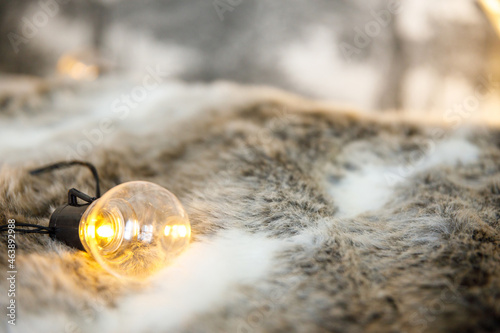 Garland lamps lie on a fluffy, cozy fur blanket. Coziness and atmospheric mood in the home interior. New Year and Christmas background. Place for text or product, copy space