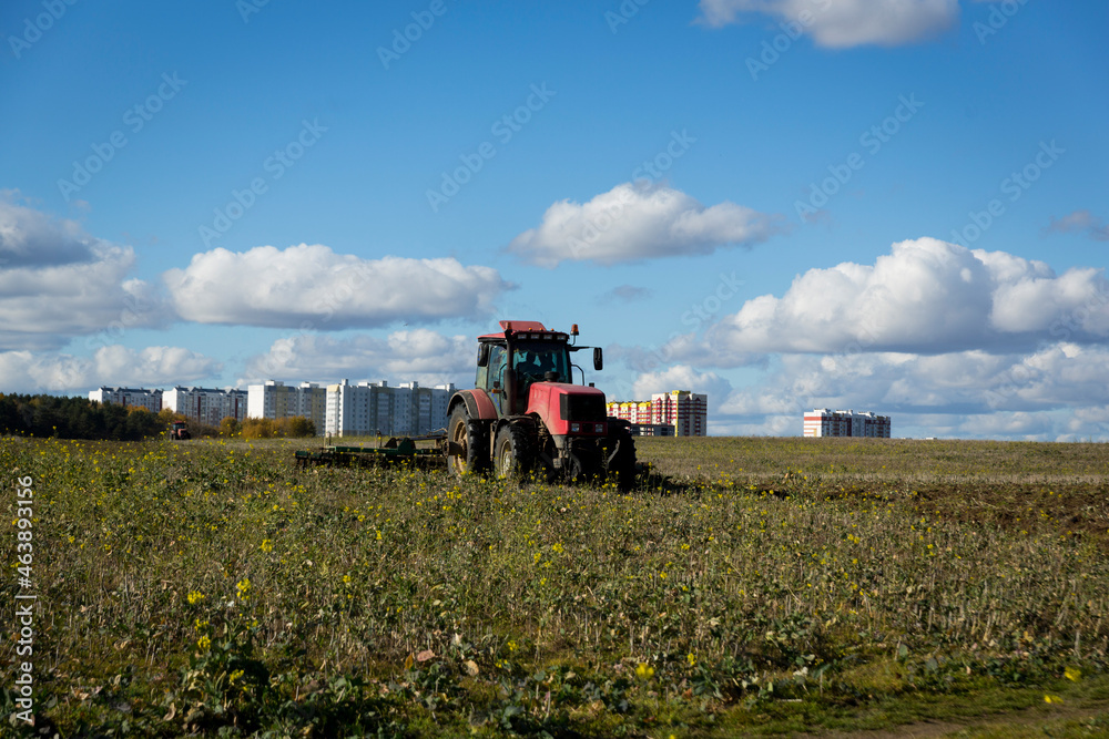 Fototapeta premium A farmer in a tractor, agricultural machinery, prepares the land with a cultivator. A modern red tractor in a field. Plowing a heavy tractor while cultivating agricultural work in a field with a plow.