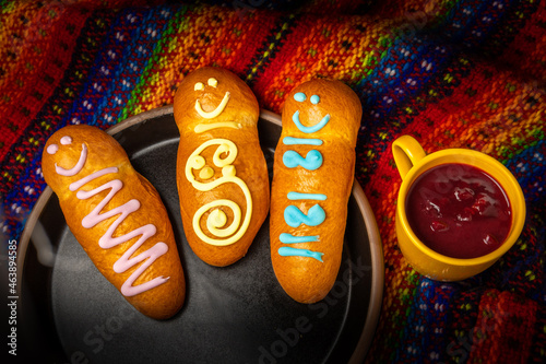 Overhead view of guaguas de pan and colada morada on a colorful tablecloth. Typical food of Ecuador on the day of the dead