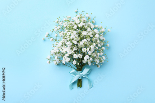 Beautiful gypsophila flowers tied with ribbon on light blue background, top view
