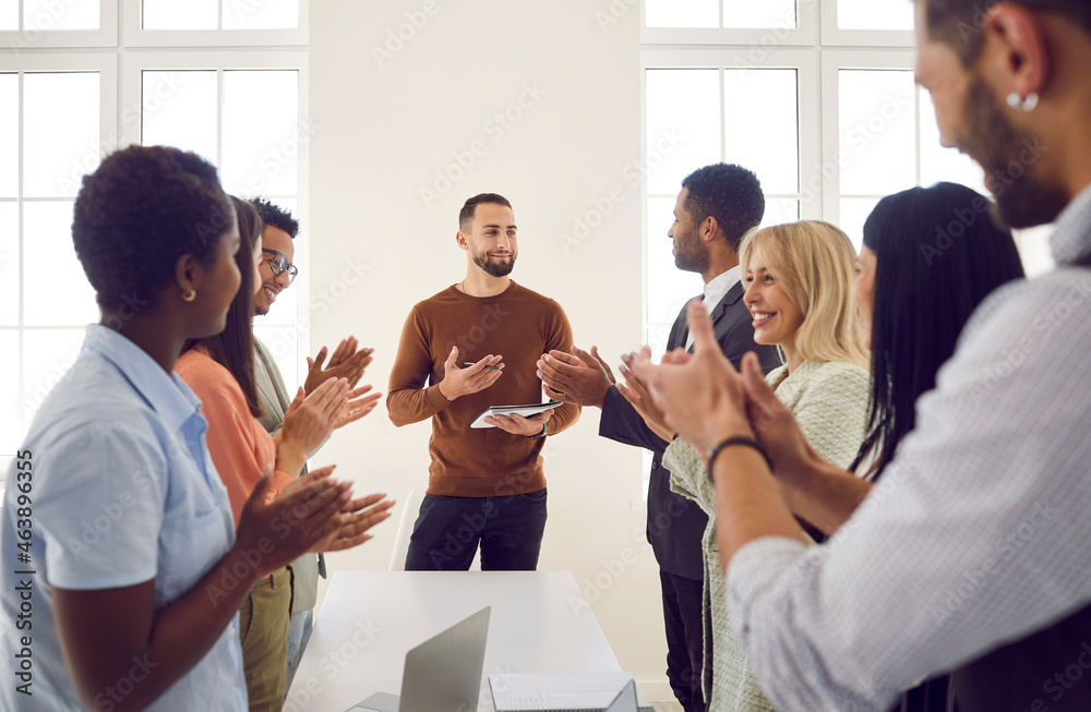 Excited businesspeople applaud successful male speaker or trainer for presentation or lesson at meeting. Happy employees clap hands show appreciation acknowledgement to team leader for speech. - obrazy, fototapety, plakaty 