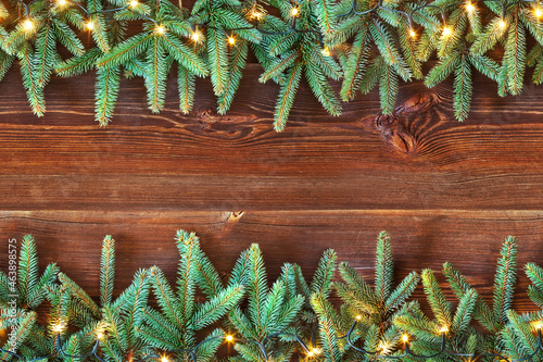 Horizontally seamless Christmas decoration of fir branches with christmast lights on rustic wooden planks. Space for text or product display. Top view. photo
