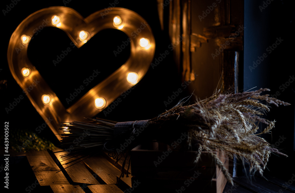 Obraz premium Autumn bouquet in a wooden box on the background of a garland. Heart of lights. Dried flowers and vegetation in home interior. Scandinavian cozy decor. Rustic.