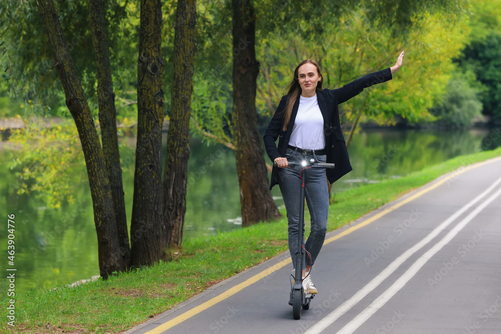 A young woman rides an electric scooter on a bike path in the park A young woman rides an electric scooter on a bike path in the park