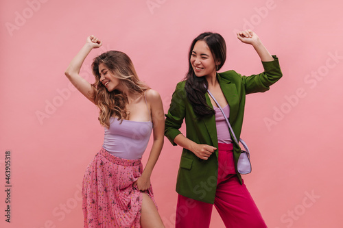 Young asian and european choreographers girls dance vigorously on background with place for text. Pretty women move to beat of music in bright summer party outfits. Active lifestyle concept