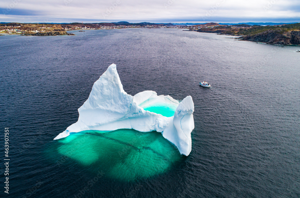 Giant iceberg near shore dwarfs a boat sailing past Giant iceberg near shore dwarfs a boat sailing past
