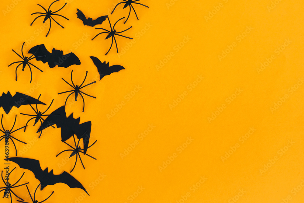 Happy Halloween. Spiders and bats flat lay on orange background with space for text. Season's greeting card. Halloween decorations border on yellow paper. Minimalist Happy Halloween. Spiders and bats flat lay on orange background with space for text. Season's greeting card. Halloween decorations border on yellow paper. Minimalist
