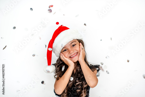 Happy New Year! cheerful funny little girl with festive confetti on a white background in a new year red cap 
