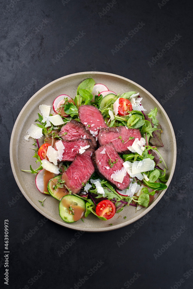 Modern style traditional fried dry aged bison beef rump steak slices with vegetable, lettuce and raspberry dressing served as top view on a Nordic design plate