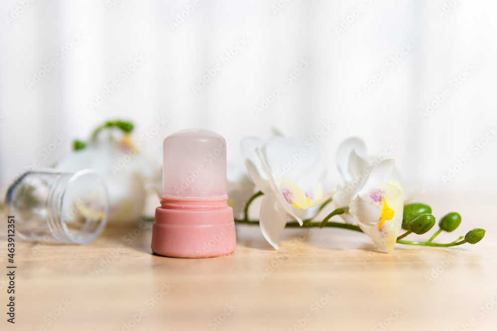 Natural eco crystal alum deodorant and orchid branch with flowers on light wooden background