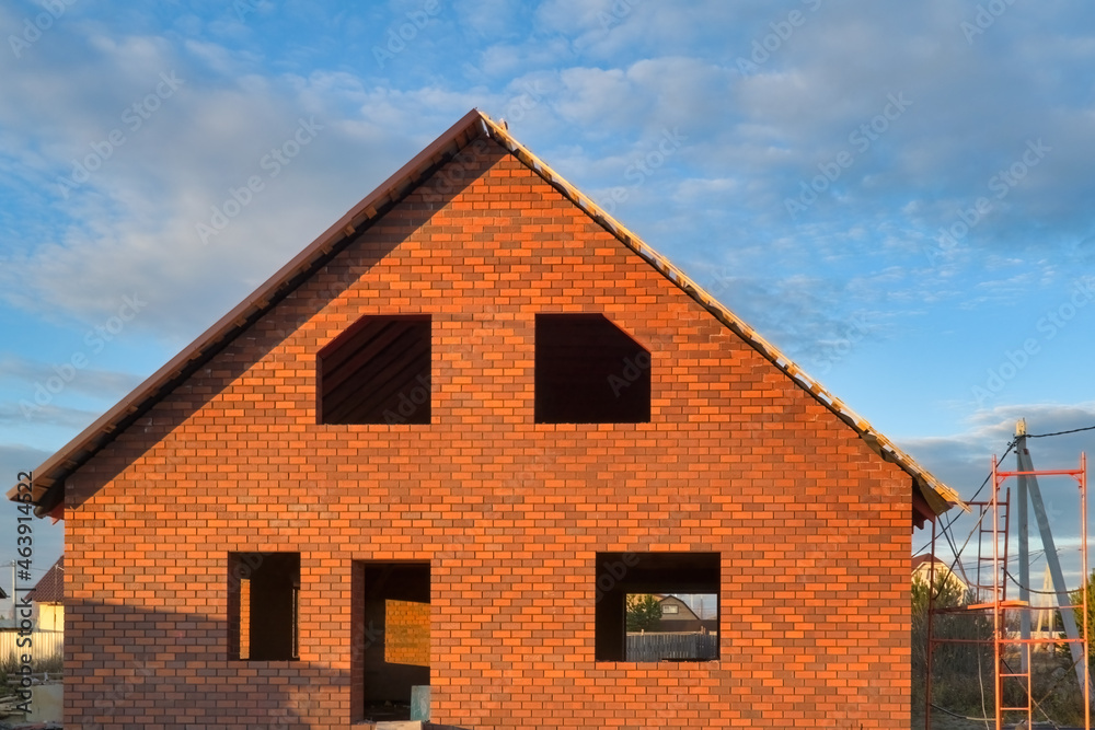 Fragment of a red brick house under construction on a background of blue sky.