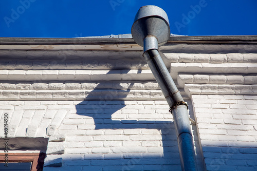 a rain gutter of a galvanized storm downspout pipe at the eaves of a building with a white facade made of white bricks on a sunny clear day. photo