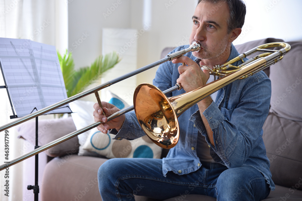 Fototapeta premium Man practicing trombone in a sofa at home