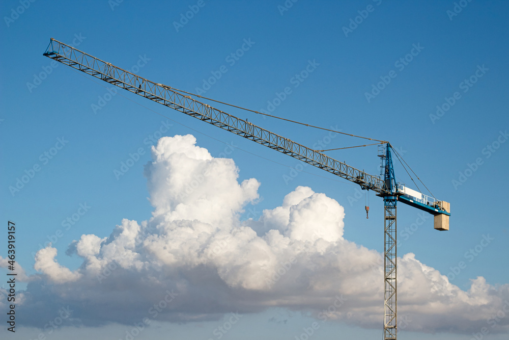 Industrial construction tower crane against a blue sky background with dramatic clouds Industrial construction tower crane against a blue sky background with dramatic clouds