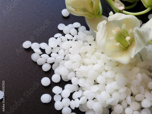 A pile of natural white beeswax pearls on a black background and white natural flower photo